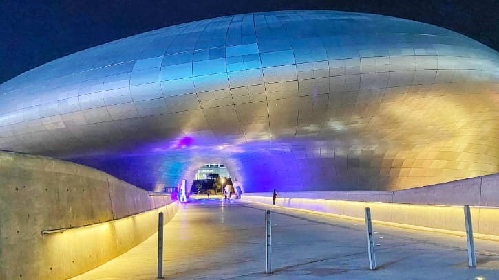 Futuristic curves of Dongdaemun Design Plaza lit up at night, a modern Seoul landmark