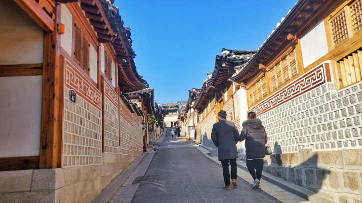 Couple strolling through Bukchon Hanok Village in Seoul, with traditional Korean houses lining the tranquil alleyway