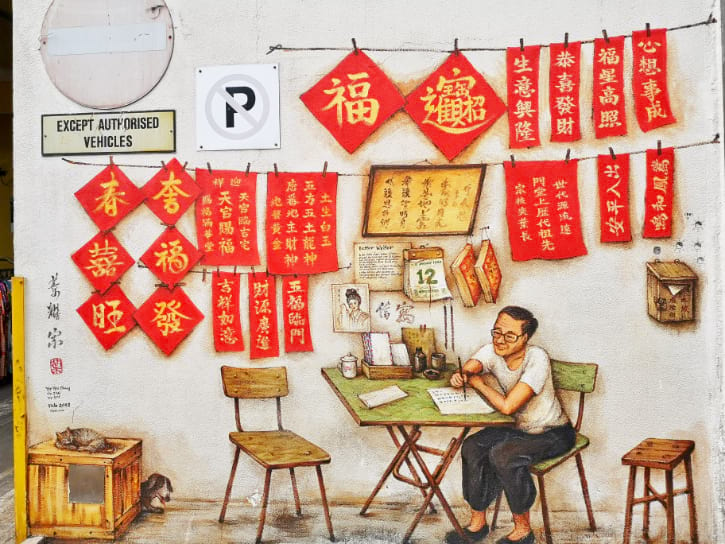 A wall mural depicting a calligrapher at work, with bright red banners and vintage Chinese posters in the background