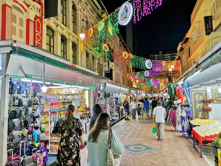 A vibrant Chinatown market with stalls and lanterns, busy with shoppers and cultural decorations