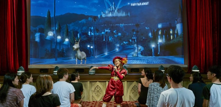 Performer engaging with audience at "Donkey Live" show, with a backdrop of an animated donkey and a magical castle