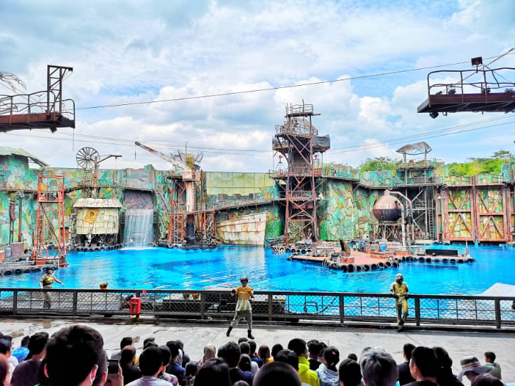 Stunt performers on a water stage with a post-apocalyptic set design at the WaterWorld show