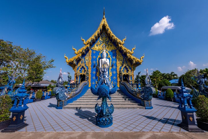 Blue and gold temple with a central statue, ornate roof, and dragon-shaped stair railings at the entrance.