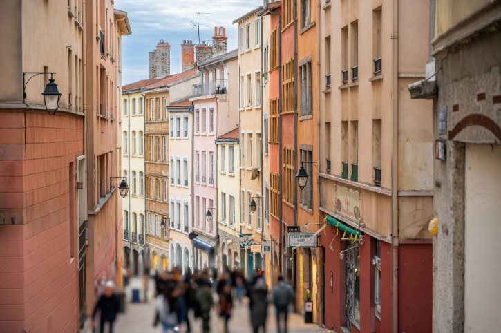 Colorful narrow street of a European town with pastel houses and people walking.