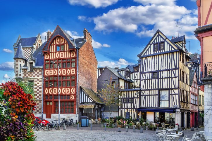 Colorful half-timbered houses line a cobblestone square under a blue sky; bicycles parked near the edge.