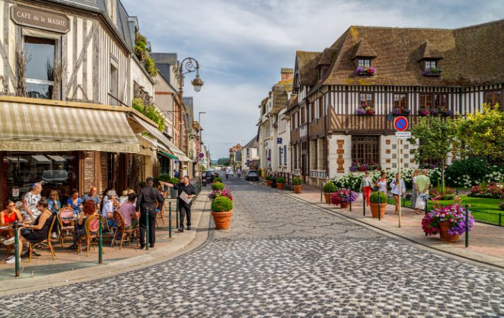 Outdoor cafe on a cobblestone street in a quaint town with half-timbered buildings and people dining at tables outside.
