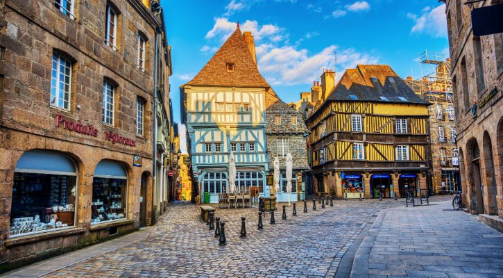 Historic European town square with timber-framed houses, cobblestone street, and outdoor seating under a blue sky.