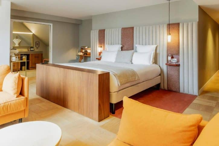 Hotel bedroom with a king bed, upholstered headboard, side tables, and an open doorway to the bathroom.